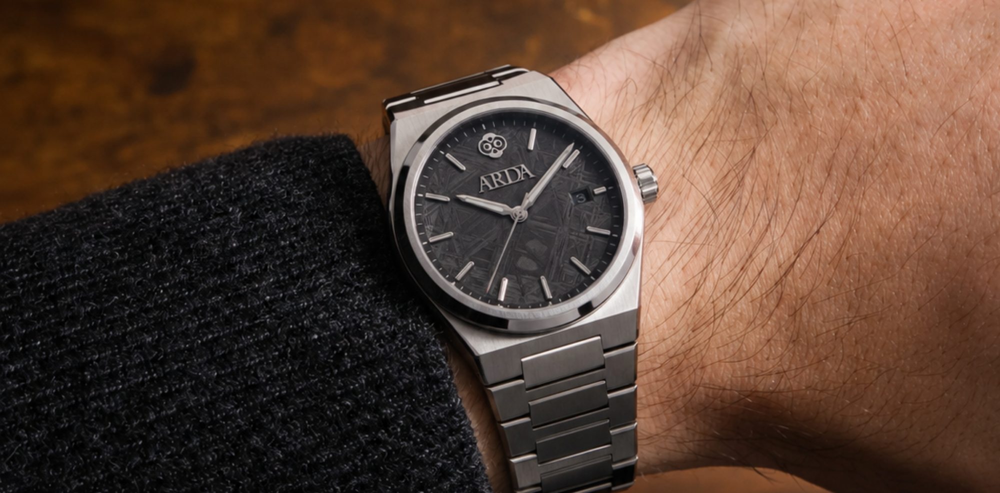 The ARDA watch worn on the wrist, meteorite dial and polished bezel caught in warm light.